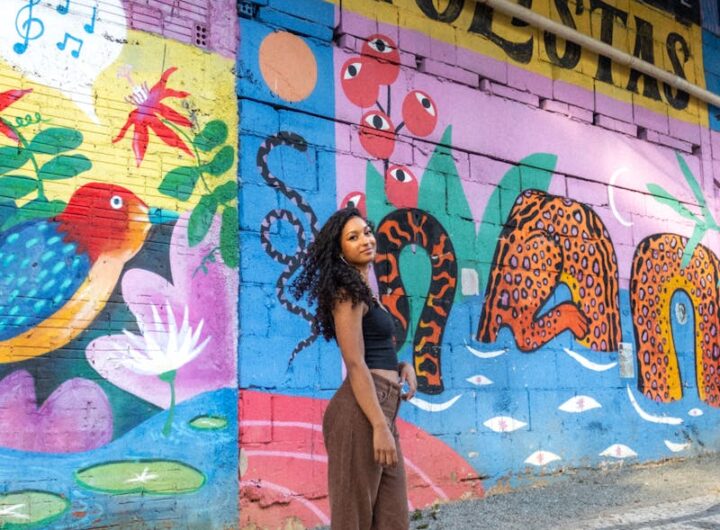 Une femme élégamment vêtue se tient devant une fresque murale vibrante avec des éléments d'art urbain dans une rue brésilienne.