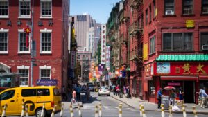Scène de rue animée en journée à Chinatown, à New York, avec des piétons, des magasins et des taxis.